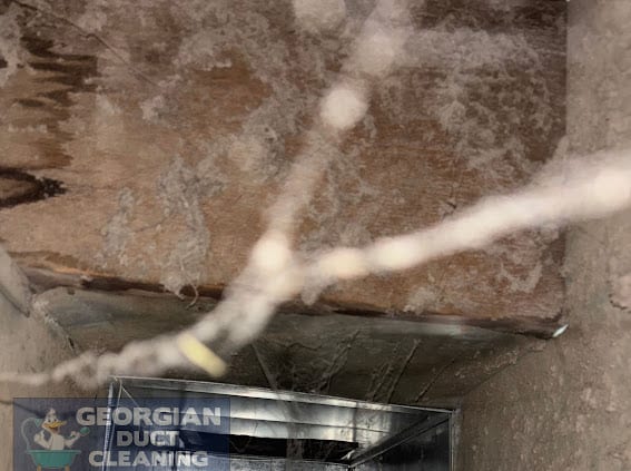 Wood-framed duct caked with dust and cobwebs before cleaning